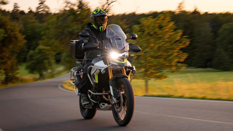 Driver riding motorcycle on empty road during sunset