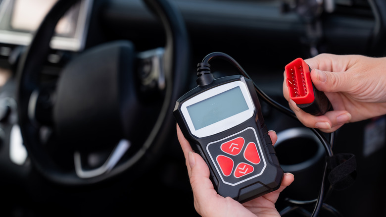 A person holding an OBD-II scanner in a car