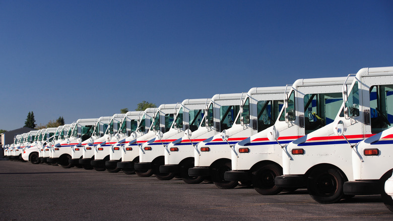 Side view of a long line of Grumman LLV mail trucks parked in a row in a parking lot