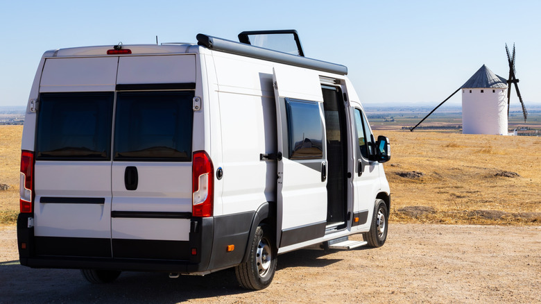Shot of a white camper van parked with a windmill in the background
