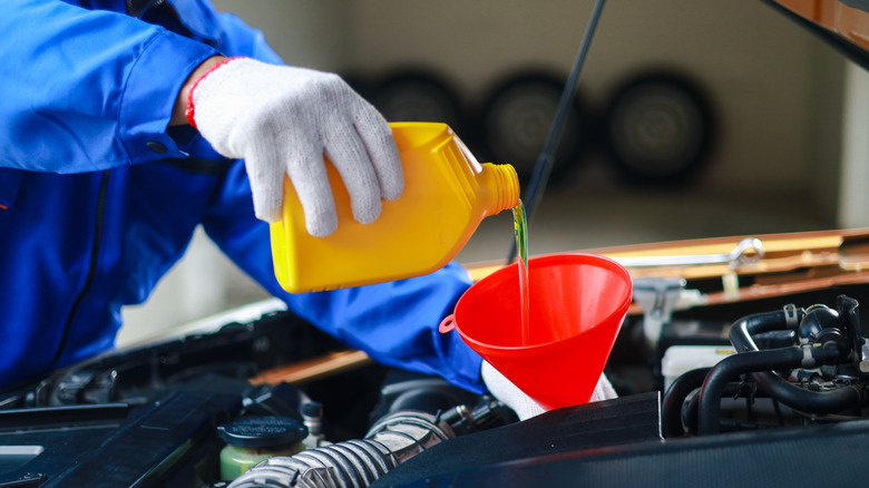 Mechanic with white gloves pouring motor oil into funnel into engine