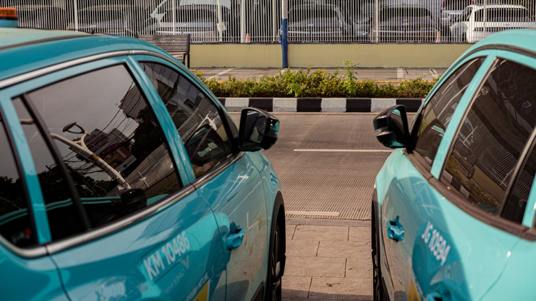 A portrait from behind, two turquoise Xanh SM online taxis from Vietnam parked on the side of the road.
