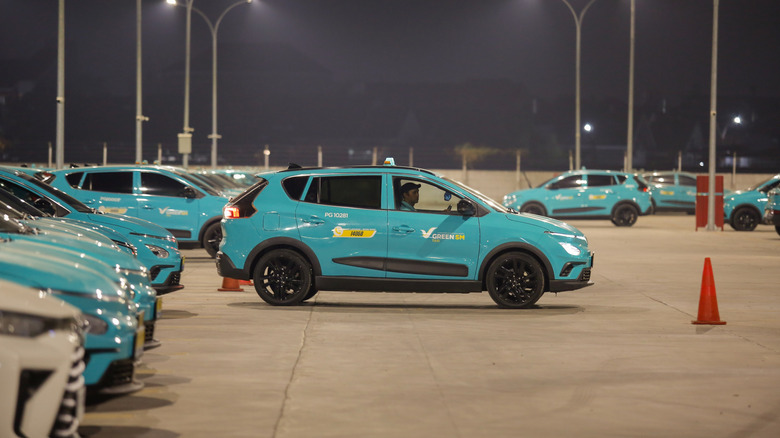 MAKASSAR, INDONESIA – OCTOBER 8, 2026: A Green SM electric taxi drives through a depot parking lot filled with rows of the company's taxis at night.  by: rhocits