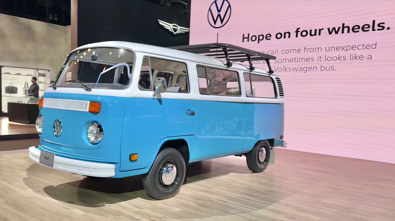 A front three quarters shot of Azul, the blue and white 1977 Volkswagen T2 parked on hard wood in front of a screen that says 
