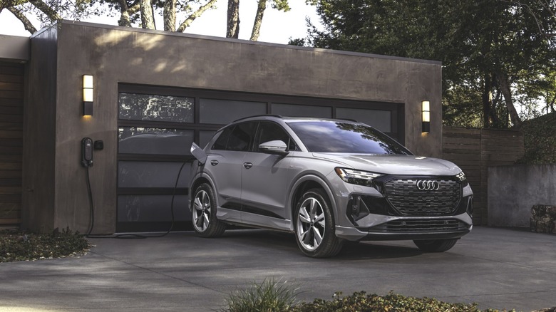 front three-quarters shot of a gray Q4 E-Tron charging in front of a concrete garage with a glass door