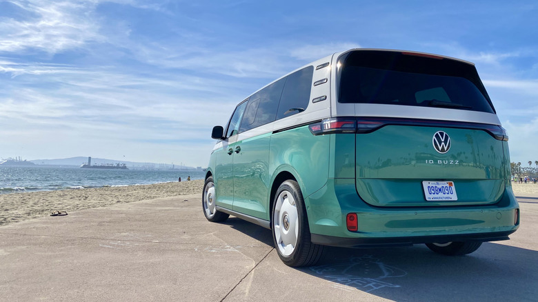 Rear three quarters shot of a Mahi Green and white ID Buzz parked on the beach with the ocean and a blue sky in th background