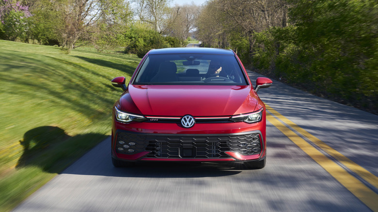 A red 2026 Volkswagen GTI being driven down a country road.