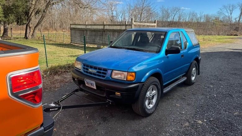 A blue Isuzu Amigo being towed behind an orange pickup