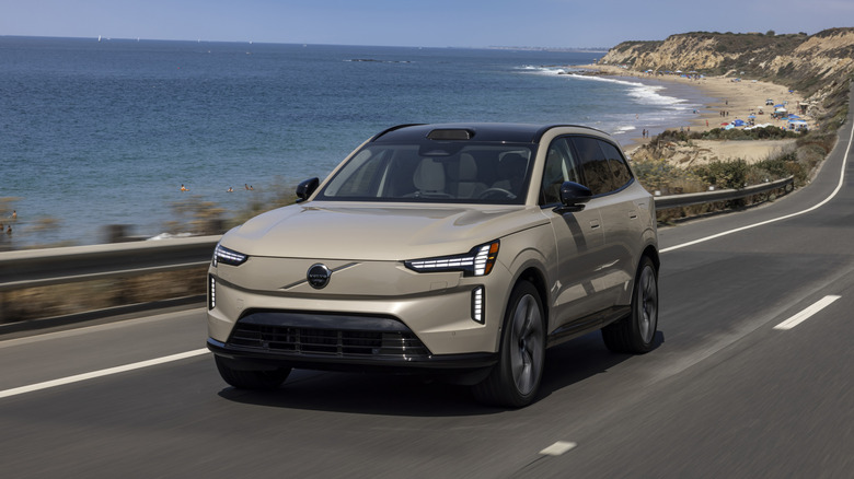 2025 Volvo EX90 driving down an oceanside road with a beach