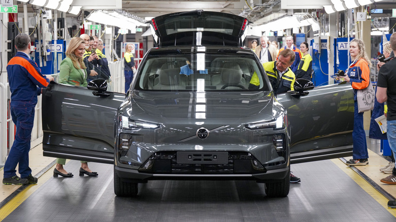 head-on shot of a gray EX60 with its doors and tailgate open on the assembly line with lots of people around it and one man getting in the driver's seat