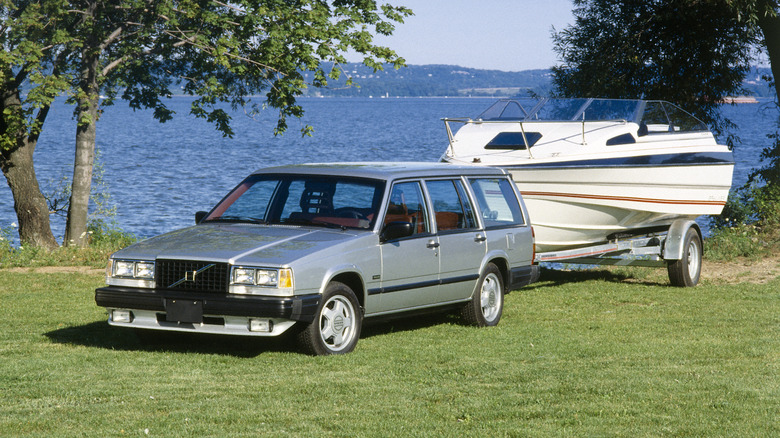 A Volvo 740 Turbo station wagon towing a yacht on grass