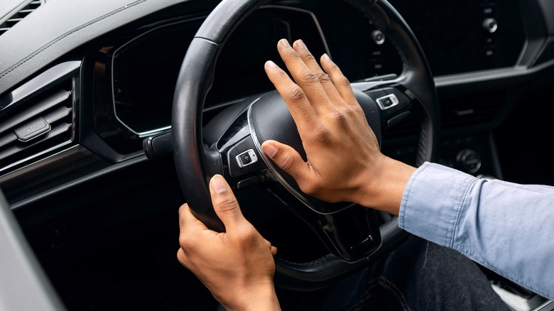 A driver honking their car horn by pressing into the center of the steering wheel.