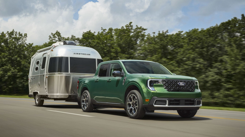 An Eruption Green 2025 Ford Maverick Hybrid AWD towing a silver Airstream trailer on a two-lane highway.