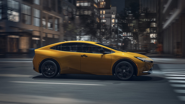 A yellow 2026 Toyota Prius Nightshade Edition driving through an urban landscape at night