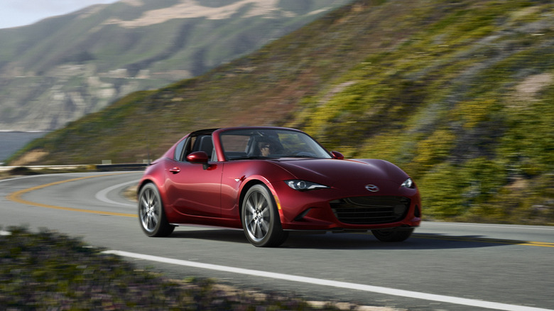 A Soul Red Crystal Mazda MX-5 Miata RF driving along a winding coastal highway with the retractable roof down.