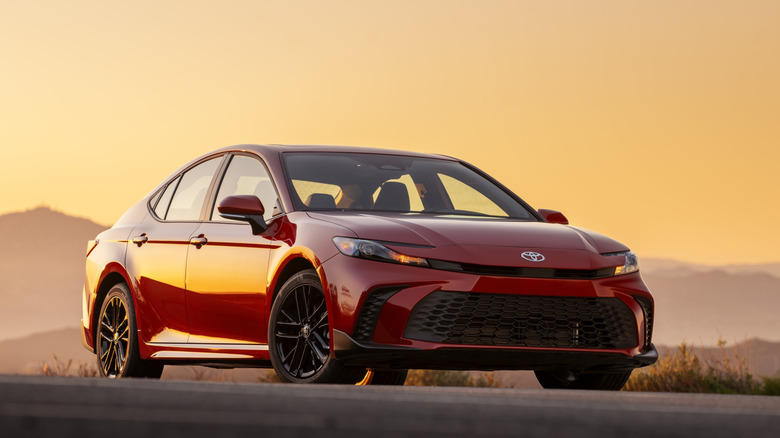 A Supersonic Red 2026 Toyota Camry SE AWD parked on a hill at sunset.