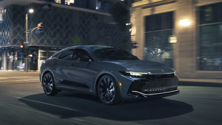 A 2026 Toyota Crown Nightshade edition in a dark grey finish driving through a city at night.