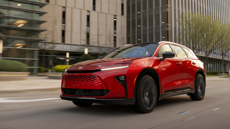A Red 2026 Toyota Crown Signia Limited SUV driving past modern office buildings.