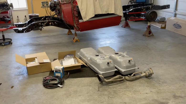 A pair of new Chevrolet side saddle fuel tanks on garage floor next to body and frame pieces