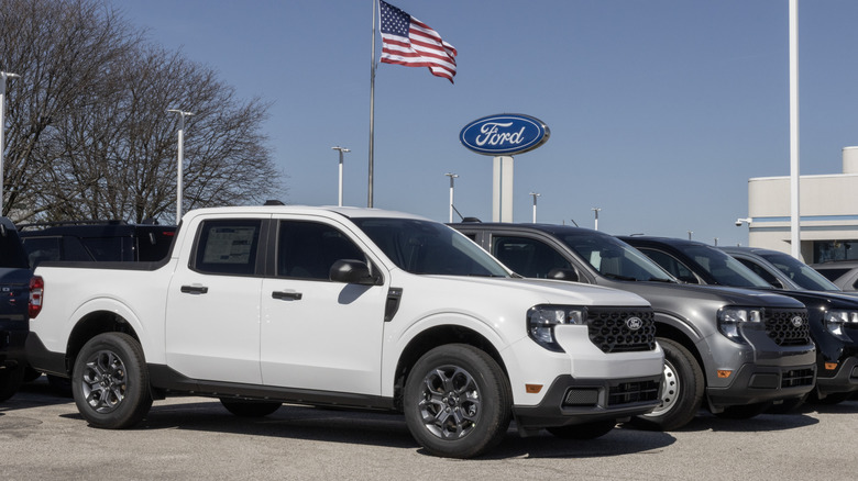 A row of fresh Ford Mavericks sitting on a dealer lot with the American flag prominently displayed in the background.