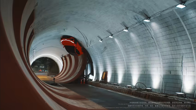 A reddish electric SUV is on the ceiling of a tunnel as it drives an upside down loop in a stunt demonstration for Chinese EV company Voyah.