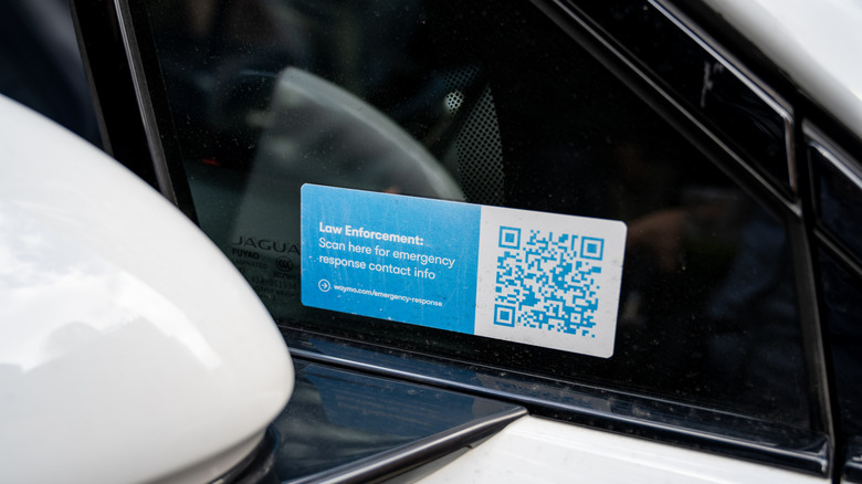 A sticker on a Waymo vehicle window, with a QR code, directing law enforcement to scan for emergency response contact information.