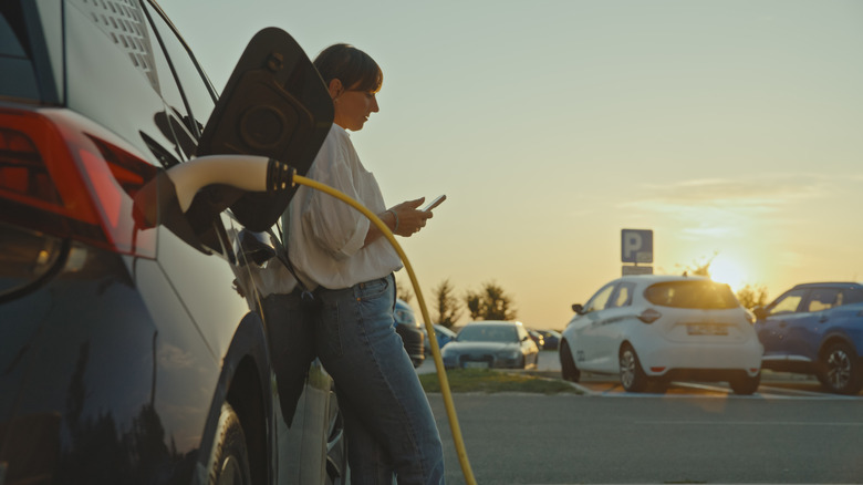 A woman scrolls her phone while recharging her EV.