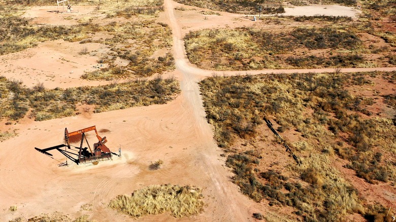 A lone oil pump sits in the Texas Permian Basin sands arid grasses with more pumps in the distance.