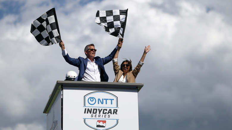 Sean Duffy, U.S. Secretary of Transportation stands on the start/finish stand at the Freedom 250 IndyCar race in Washington DC in 2026 waving the checkered flags.