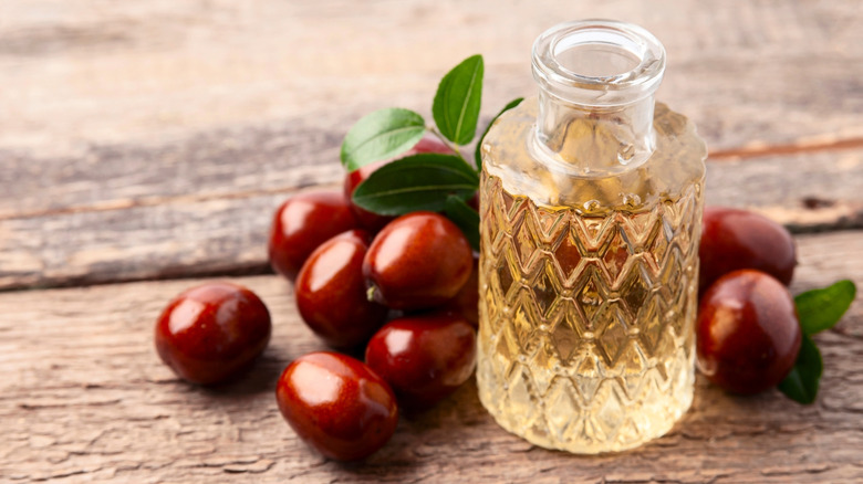 A bottle of jojoba oil and jojoba fruits on a wooden table