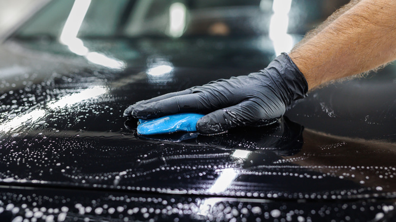 A detailer using a clay bar on the car's hood