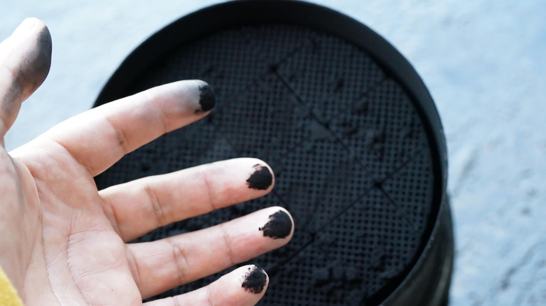 A person's dirty hand over a clogged DPF filter housing.