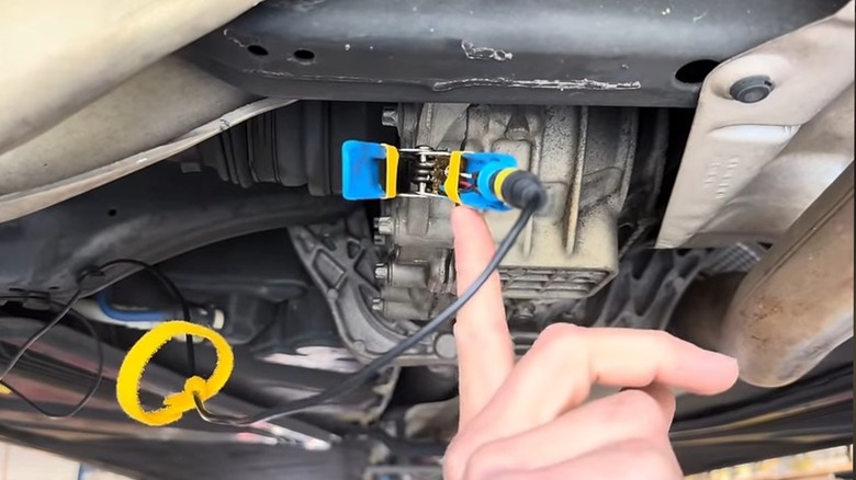 A mechanic pointing to the clamp of a vibration sensing clamp, used to diagnose the noises of a vehicle.