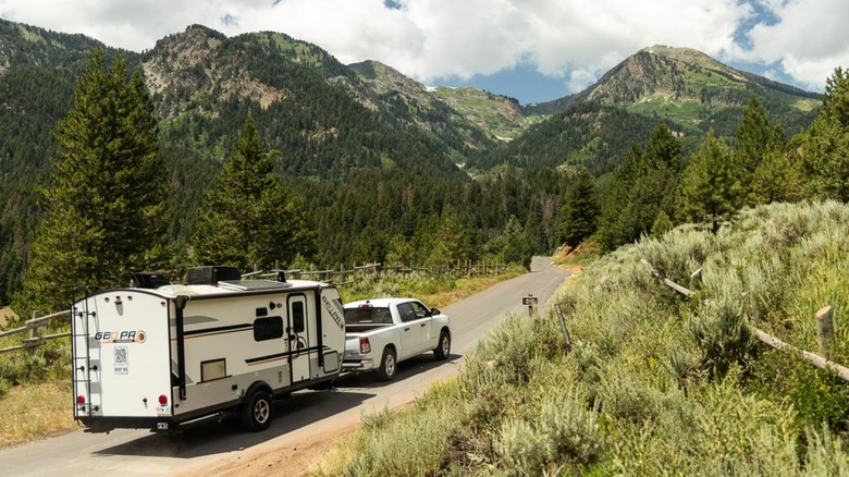 A camping trailer is being towed up a mountain road bordered by lush greenery.