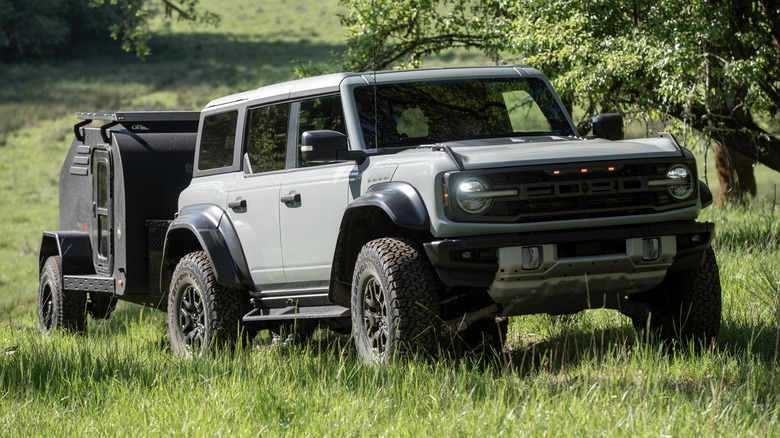 A Ford Bronco Raptor towing a trailer over grass fields.