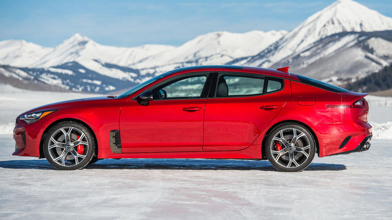 The driver's side view of 2021 Kia Stinger parked on a snowy surface with mountains in the background
