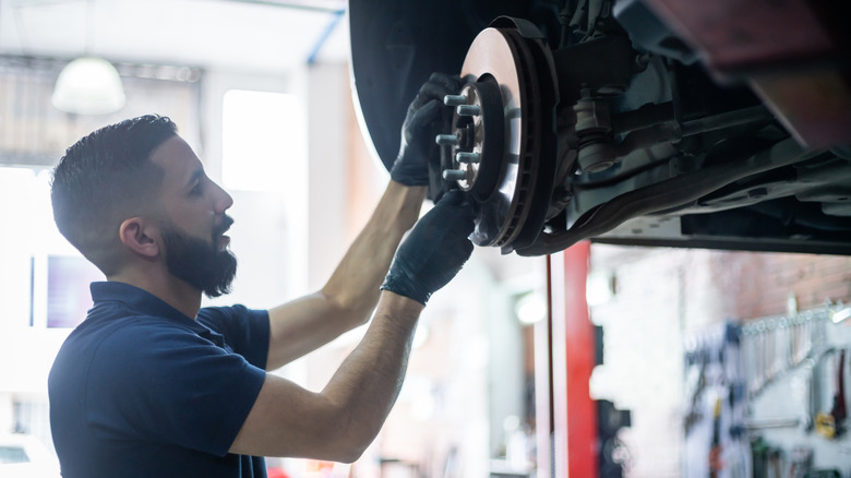 A young male mechanic wearing gloves and working on a car's brake assembly.