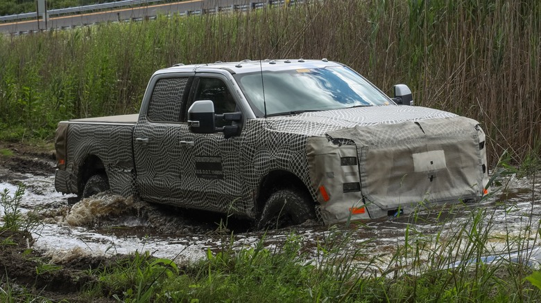 A Ford Super Duty driving through mud with a covering on