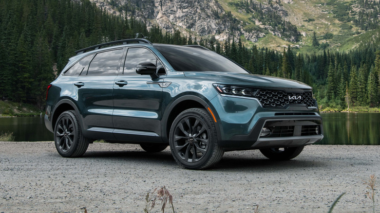 3/4 view of a 2023 Kia Sorento X-Line parked on a gravely surface with a body of water and mountain behind
