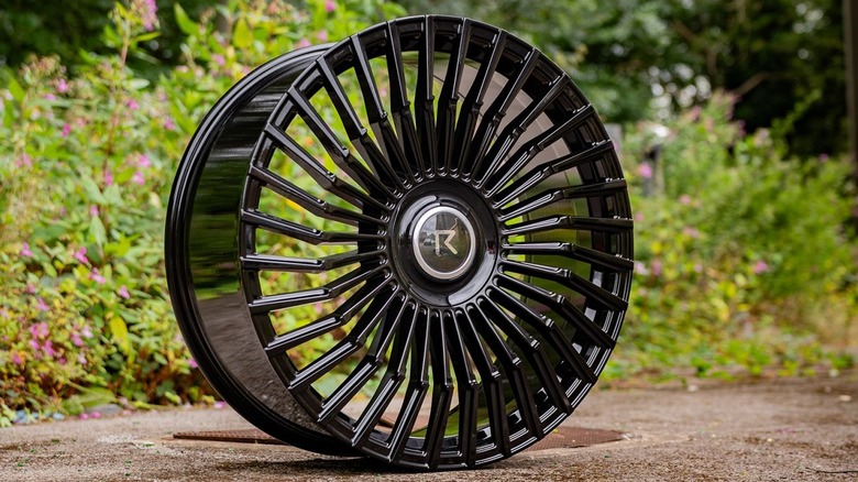 Black forged Riviera alloy wheel in front of shrubbery