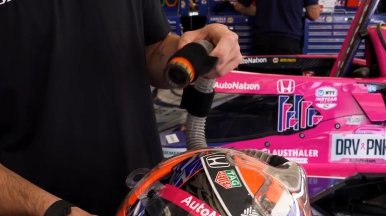Driver Alexander Rossi points holds part of the cooling tube system on a helmet