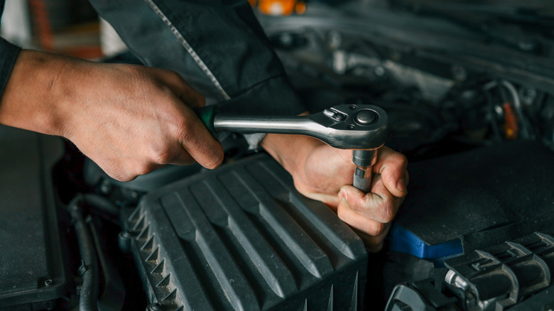 A mechanic tightening a bolt on a car engine using a ratchet wrench in a professional workshop setting.