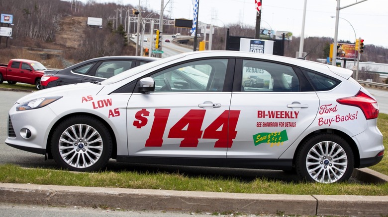 A car with a low bi-monthly payment price painted on side, parked at dealer lot