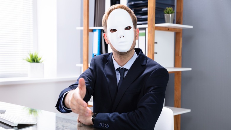A car salesman wearing white mask and a suit extending hand for a handshake