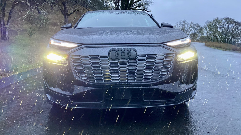 A head-on shot of a gray Audi SQ6 E-Tron with its headlights on in the rain