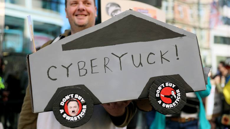 LONDON, ENGLAND - APRIL 5: A demonstrator holds a sign in the shape of a Cybertruck during a rally against Tesla CEO Elon Musk, US President Donald Trump and their recent policies outside Tesla, Oxford Street on April 05, 2025 in London, England. The London 'Hands Off' action group says that Donald Trump and Elon Musk think everything belongs to them and Londoners are fighting back! US citizens, Canadians, Brits, and people from all over the globe who've found a home in London are standing up for democracy. They believe that the US is threatening to invade Canada, Greenland, and Panama and are protesting as the Hands Off group in response. (Photo by Alishia Abodunde/Getty Images)