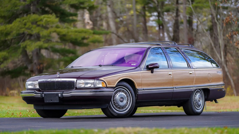 Front three-quarters shot of an immaculate maroon Roadmaster Estate Wagon parked in front of grass and trees