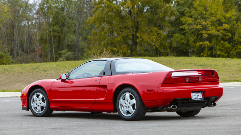 A rear three-quarters shot of a red first-gen Acura NSX parked in front of grass and trees