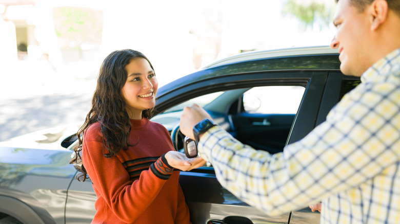 Father hands daughter the keys to an SUV for driving.