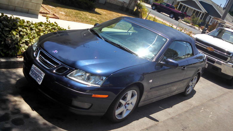 front three-quarters shot of my blue on blue Saab 9-3 cabriolet parked on the street in front of a white Silverado